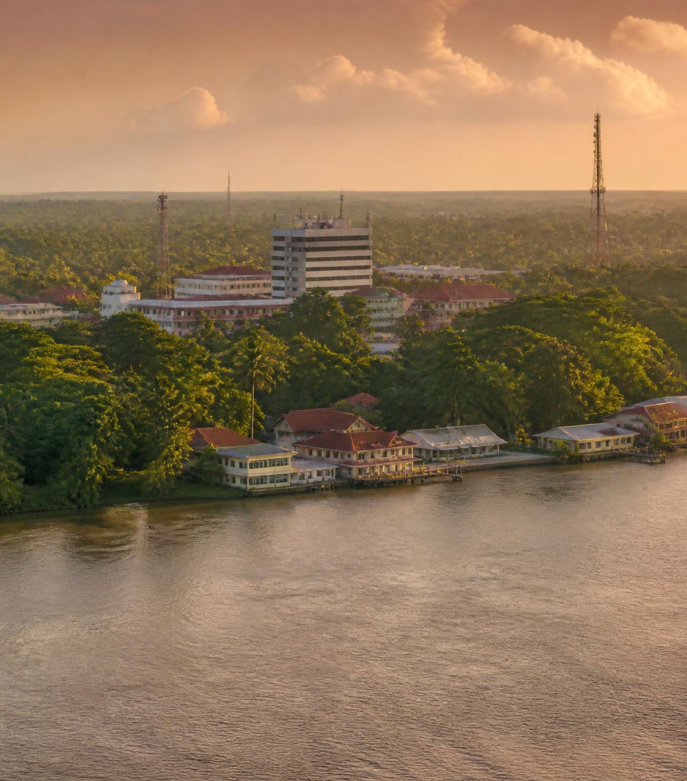 Warm evening light over a Suriname river city with rainforest and regional commercial buildings